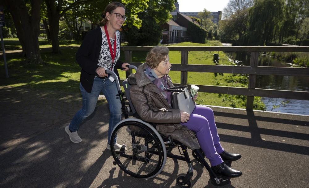 Persoon duwt dame in rolstoel over bruggetje