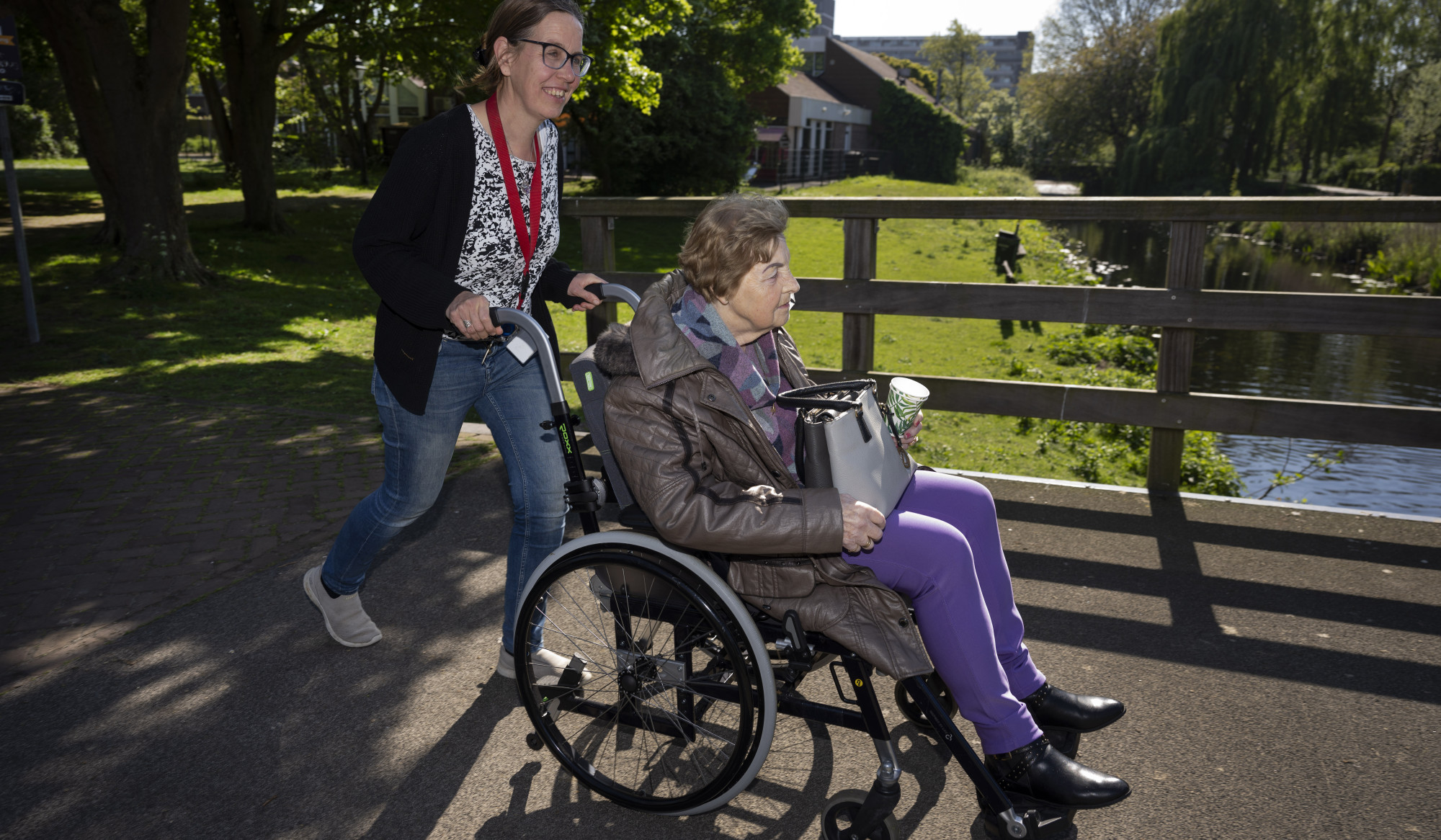 Persoon duwt dame in rolstoel over bruggetje Persoon duwt dame in rolstoel over bruggetje